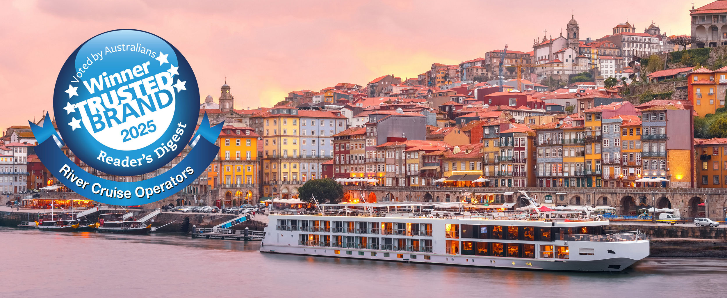 River cruise ship docked by colorful cityscape at sunset