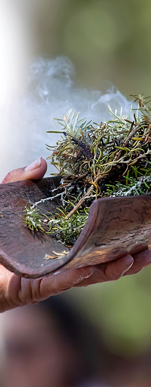 Hand holding smoking herbs in wooden vessel