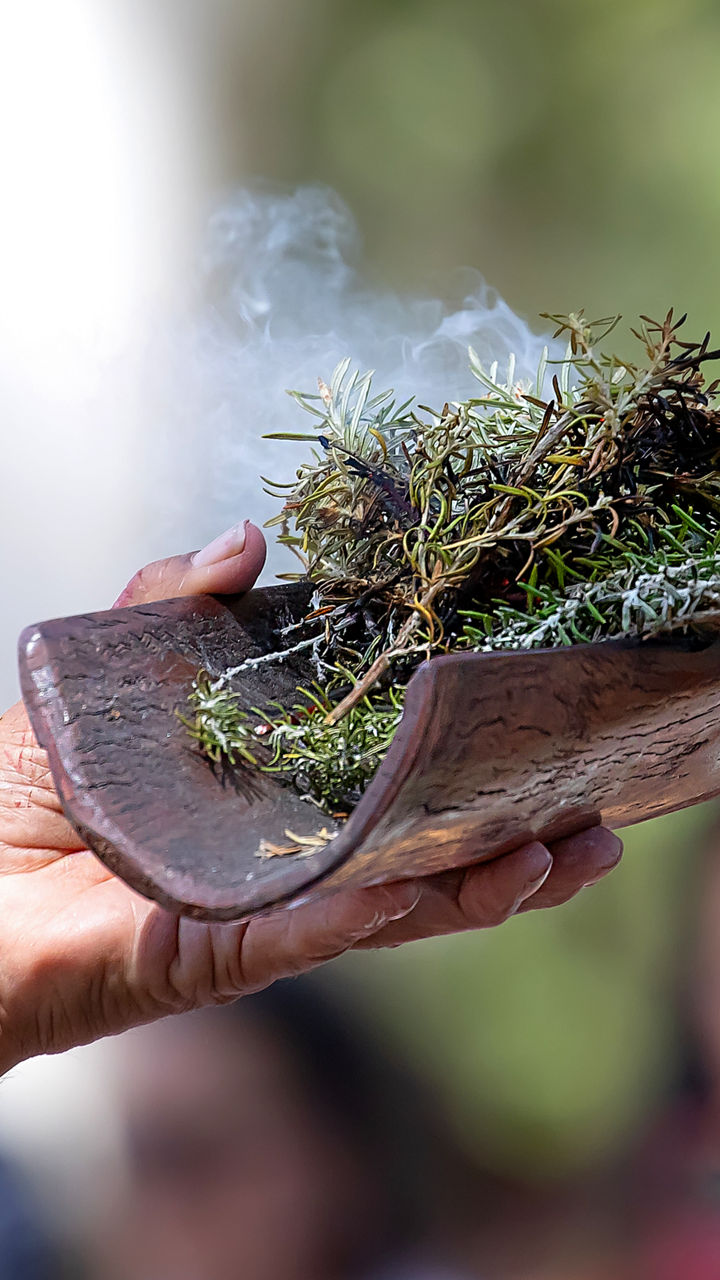 Hand holding smoking herbs in wooden vessel