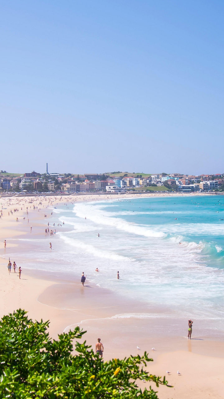 Sunny beach with waves and distant crowd