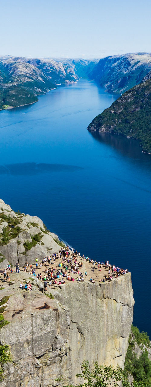 Tourists on cliff above deep blue fjord