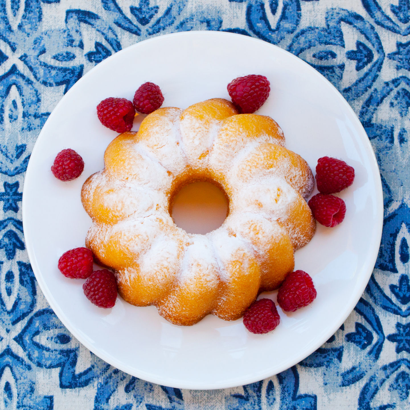 Bundt cake with raspberries on patterned tablecloth