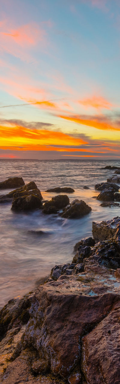 Coastal lighthouse at sunset with rocky shore