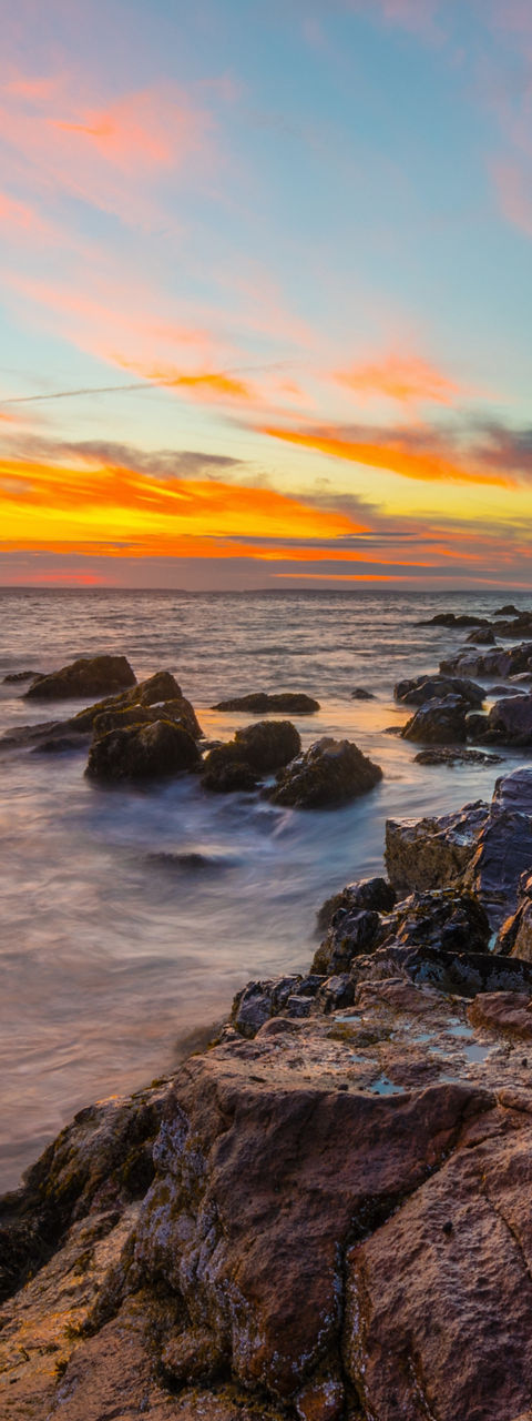 Coastal lighthouse at sunset with rocky shore