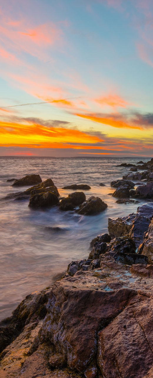 Coastal lighthouse at sunset with rocky shore
