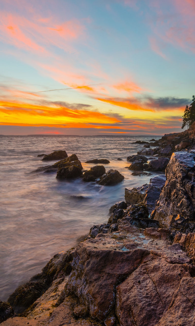 Coastal lighthouse at sunset with rocky shore