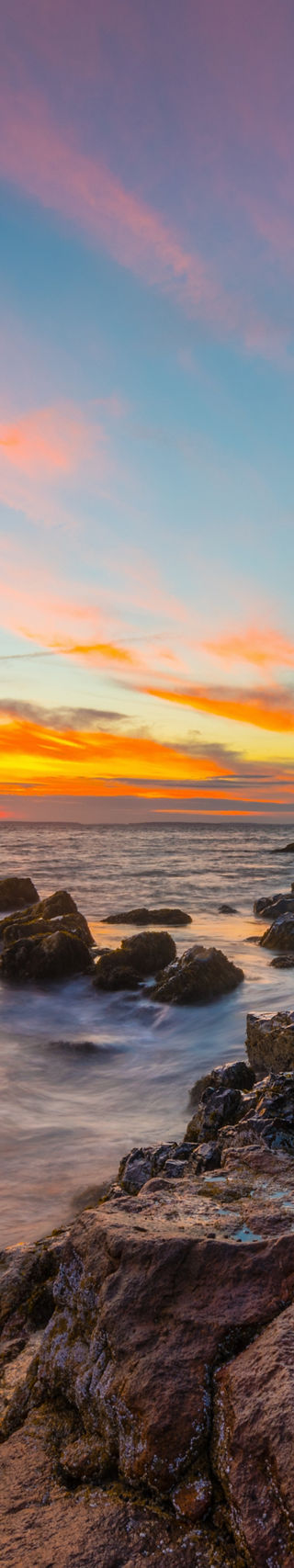 Coastal lighthouse at sunset with rocky shore