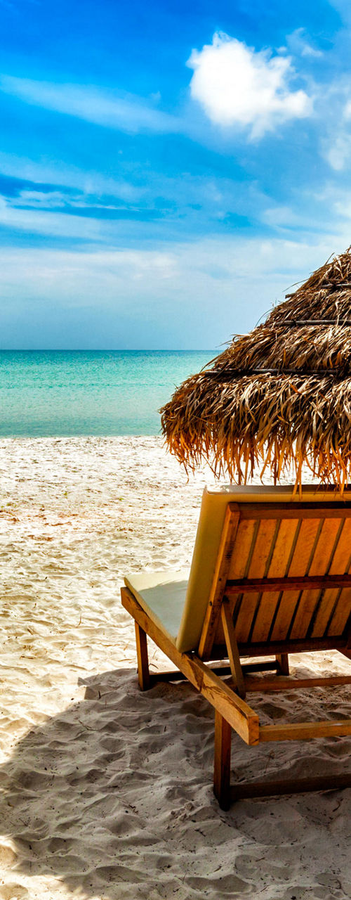 Tropical beach with straw umbrella and chairs