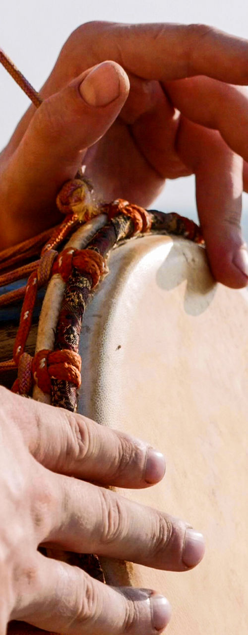 Person Playing Hand Drum on Sandy Beach Shore