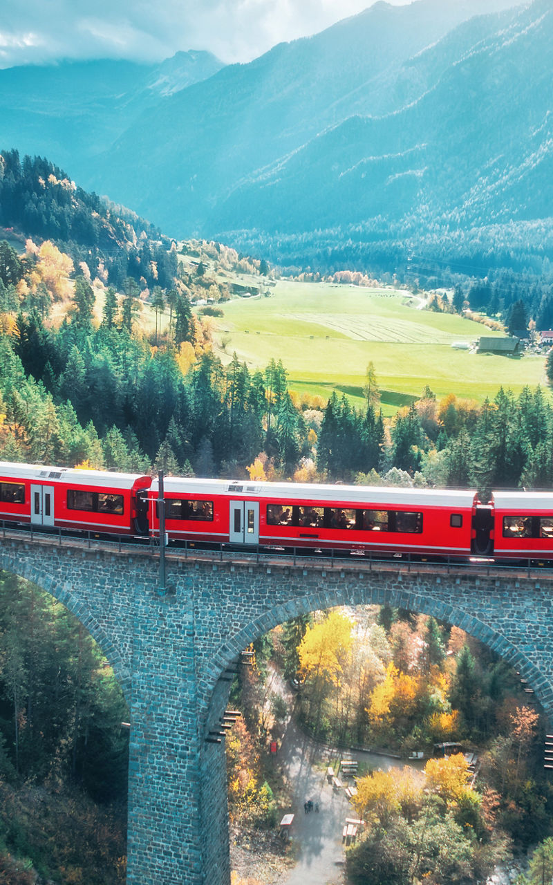 Red train crossing scenic mountain viaduct