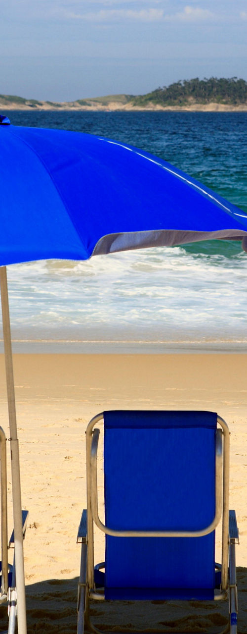 Blue beach umbrella with chairs on shore