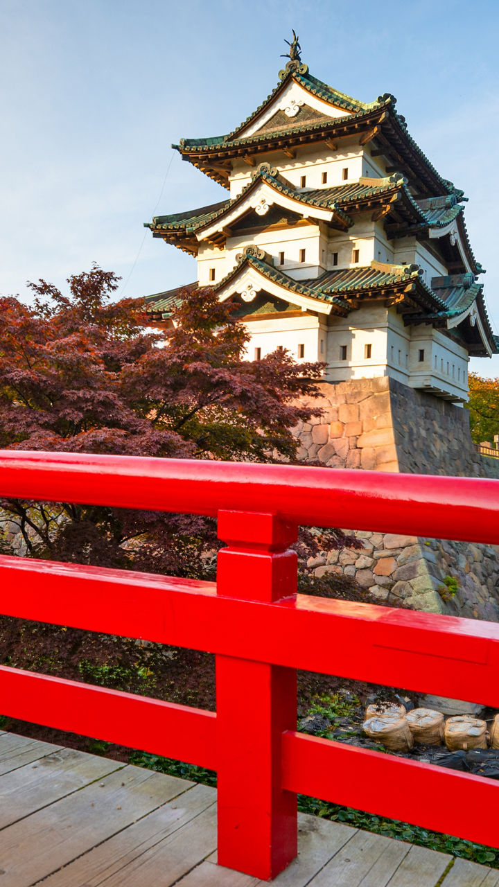 Traditional Japanese castle behind vibrant red bridge