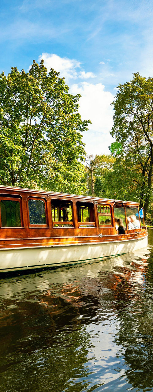 Scenic river cruise boat passing under leafy trees