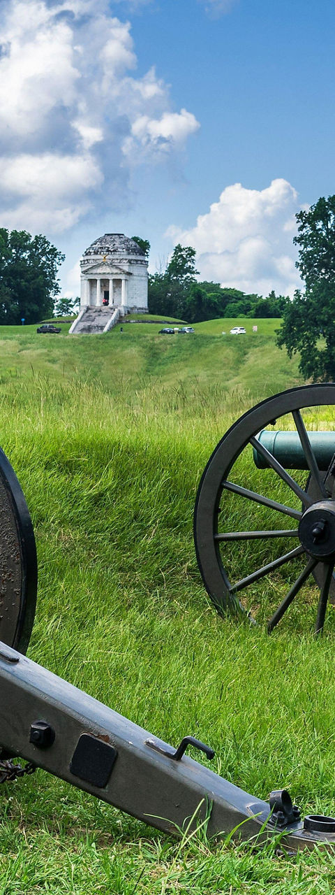 Historic cannons on grassy battlefield under blue sky