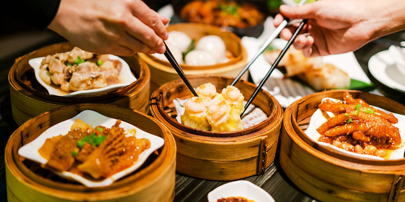 Hands sharing dim sum dishes at dinner