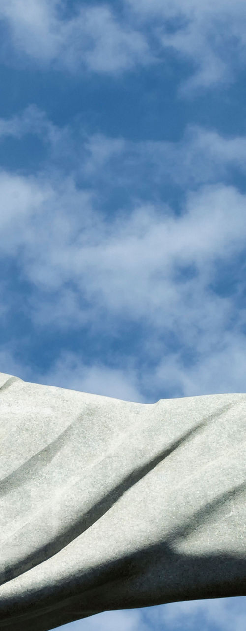 Statue with outstretched arms against sky