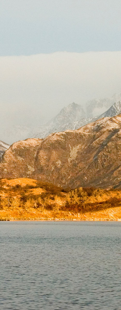Snow-capped mountains and golden hills by lake