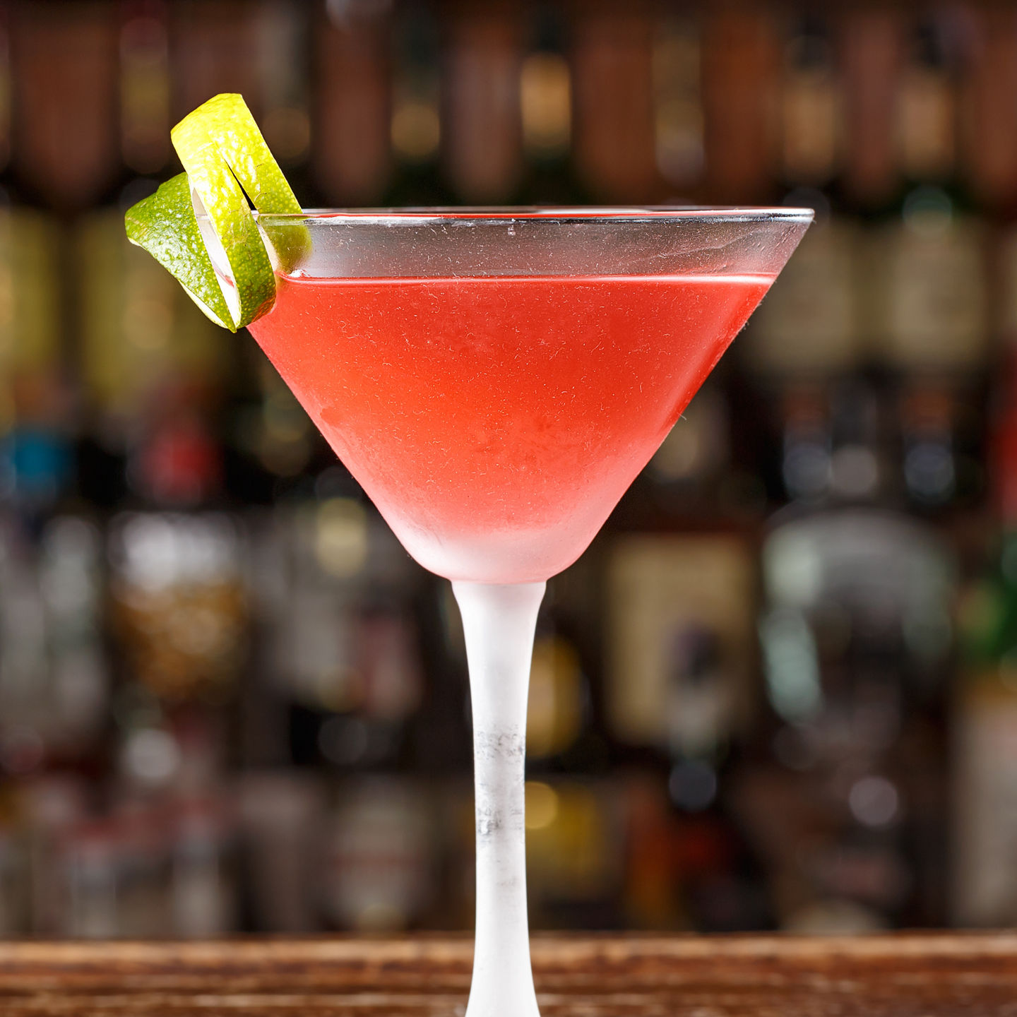 Red cocktail with lime garnish in bar setting