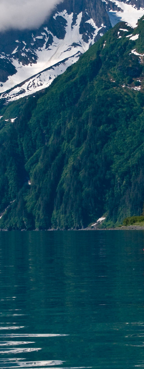 Kayakers on tranquil lake below snowy mountains