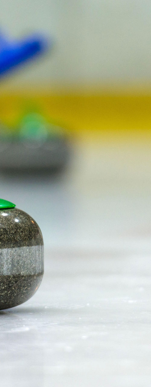 Curling stone on ice with players