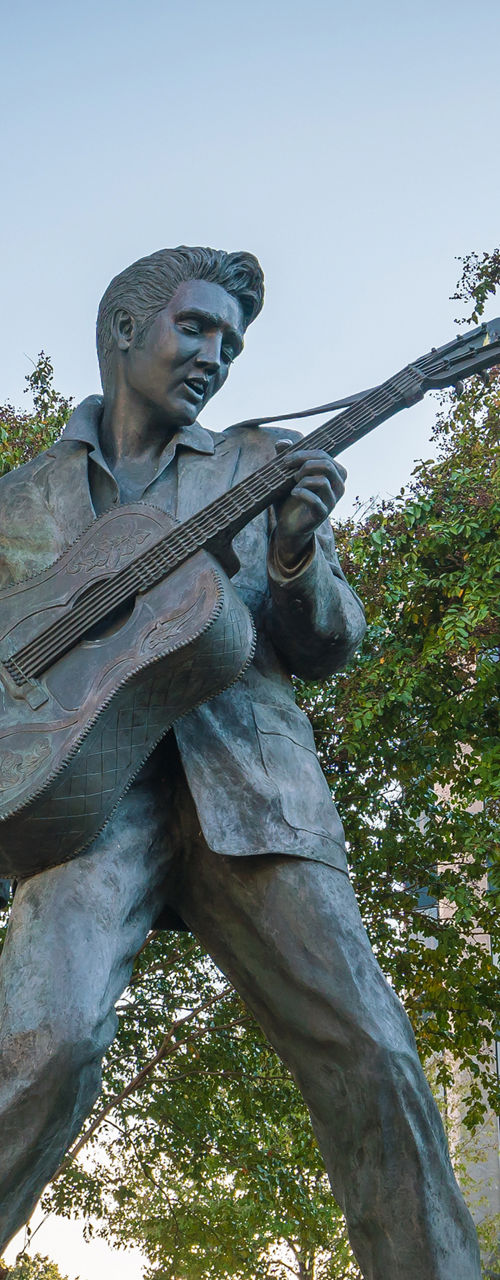 Bronze statue of musician with guitar outdoors