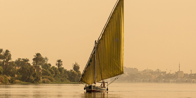 Traditional sailboat on calm river at sunset