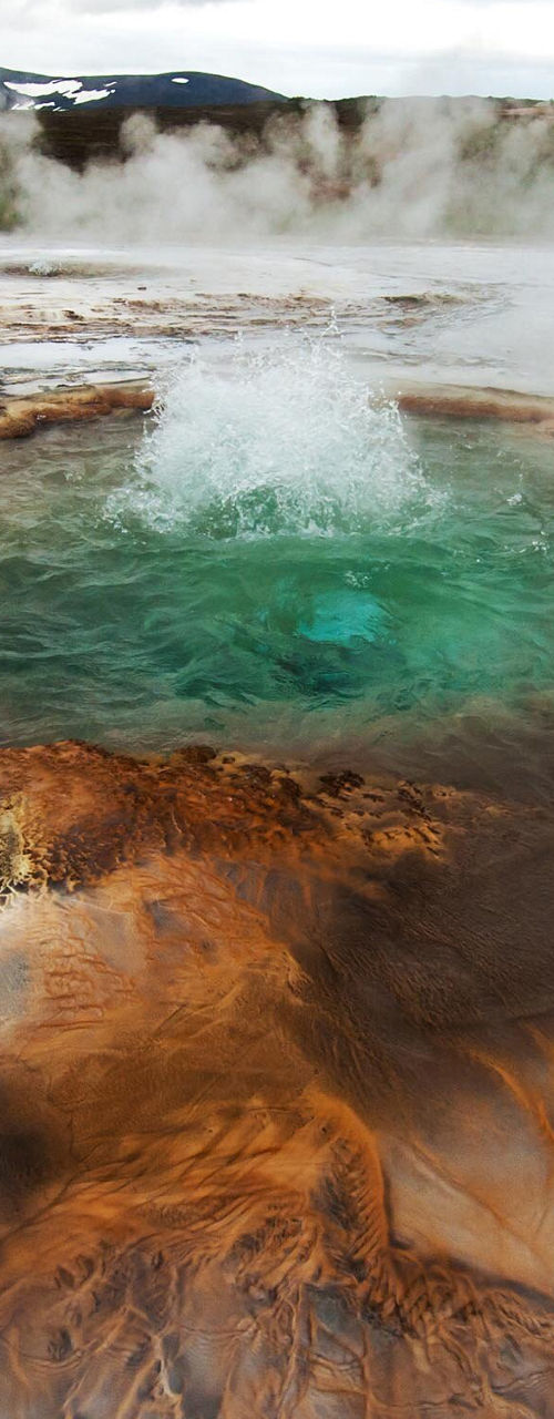 Steaming geothermal pool in rugged landscape