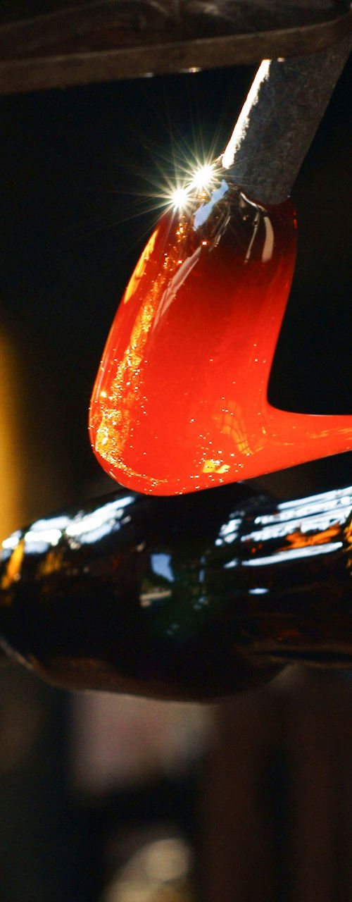 Glassblower shaping molten glass with metal tool