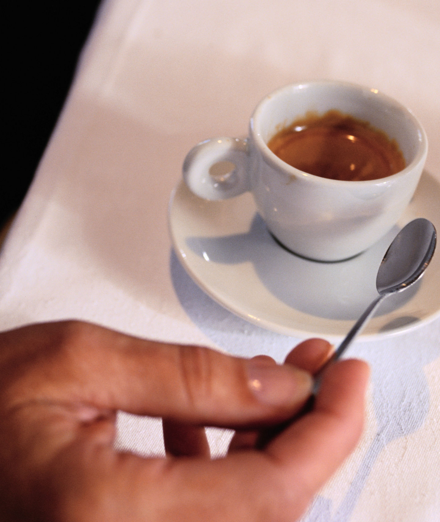 Hand holding spoon with espresso cup