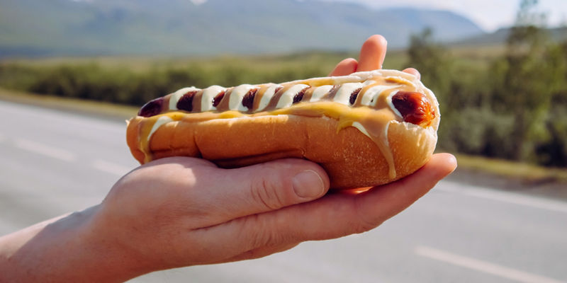 Hand holding hot dog on roadside