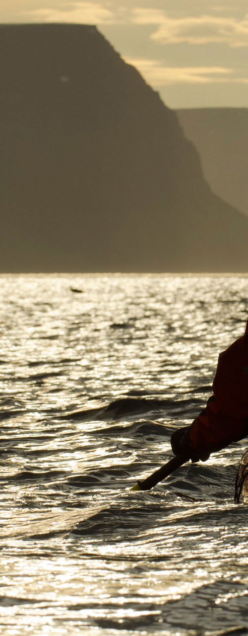 Kayaker paddling at sunset near cliffs