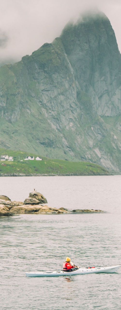 Kayakers near red cabins in scenic fjord