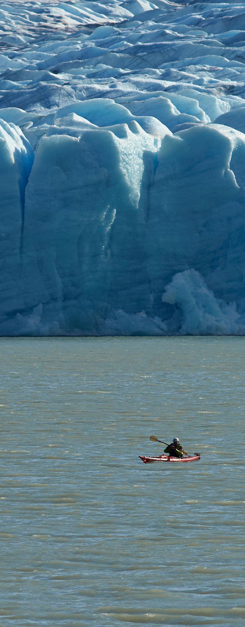 Kayakers near massive blue glacier wall