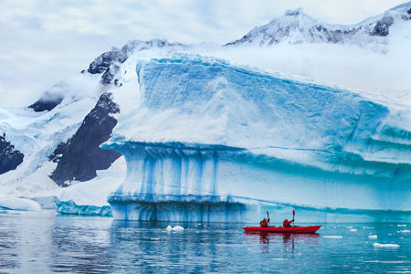 Red kayak near massive blue iceberg