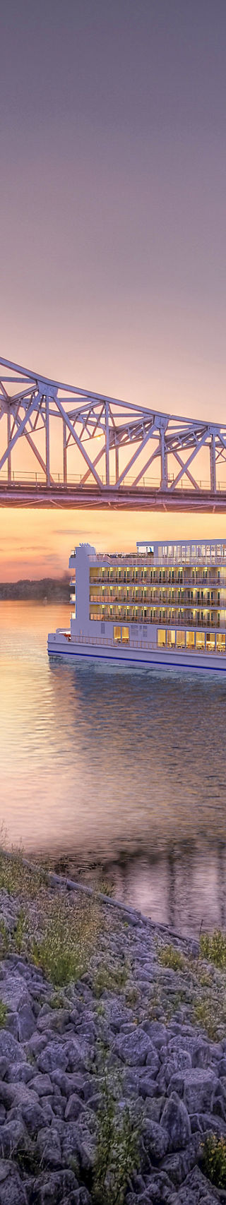 Luxury river cruise under steel bridge at sunset