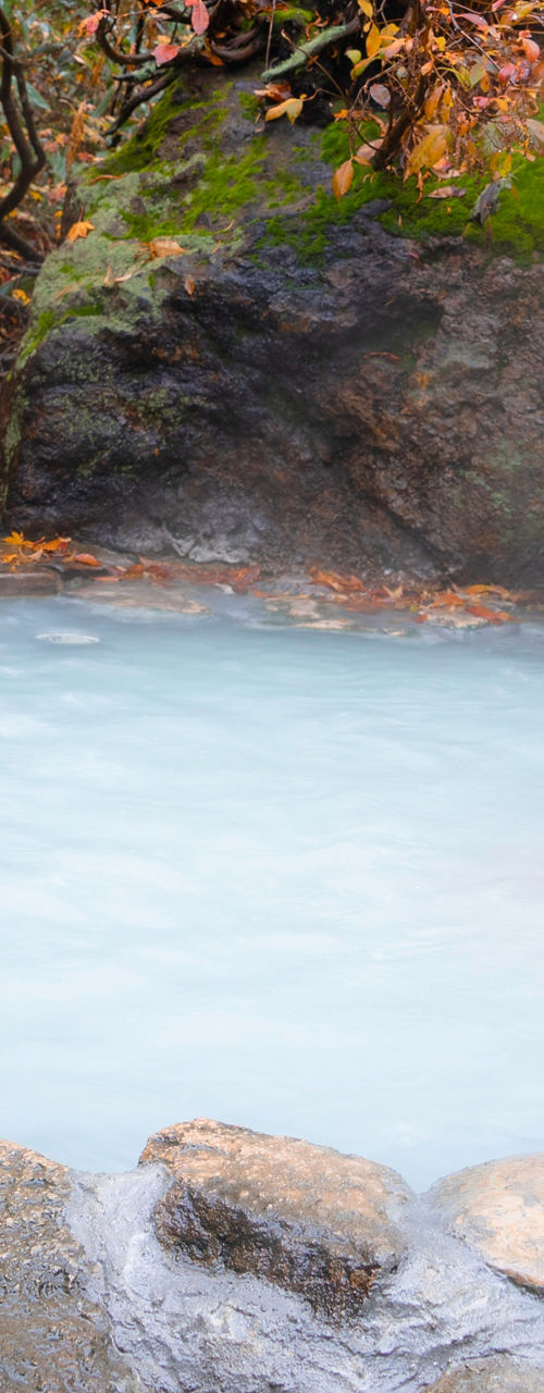Person relaxing in outdoor hot spring during autumn