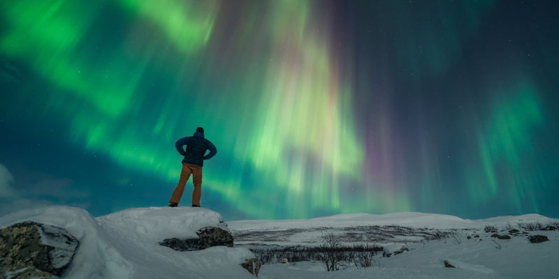 Man watching vibrant northern lights in snow