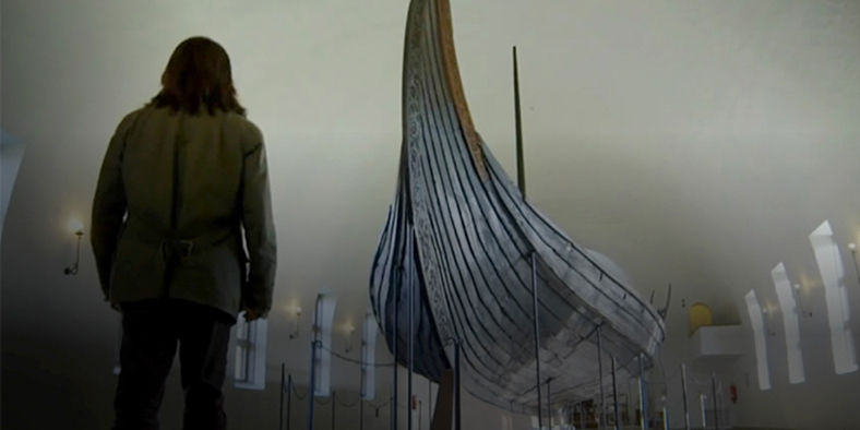 Man observing Viking ship in museum