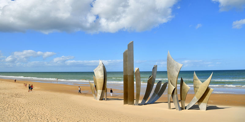 Modern sculpture on sandy beach under blue sky