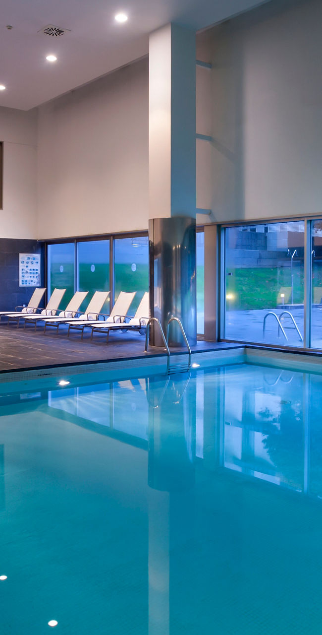 Modern indoor swimming pool with lounge chairs and windows