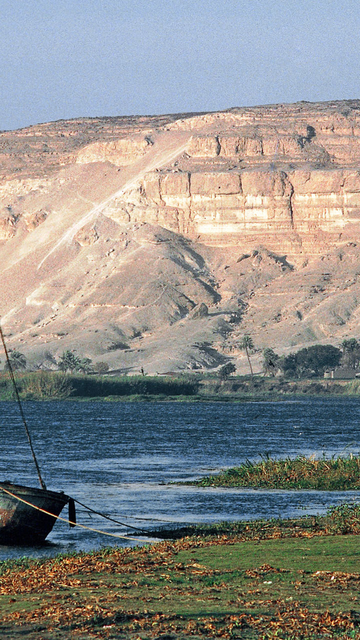 Sailboat moored on riverbank near cliffs