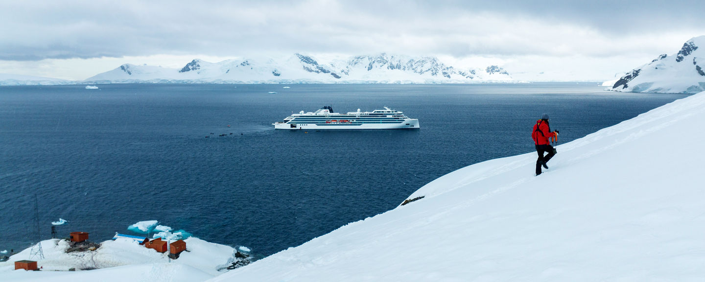 Explorer hiking snowy slope near Antarctic cruise