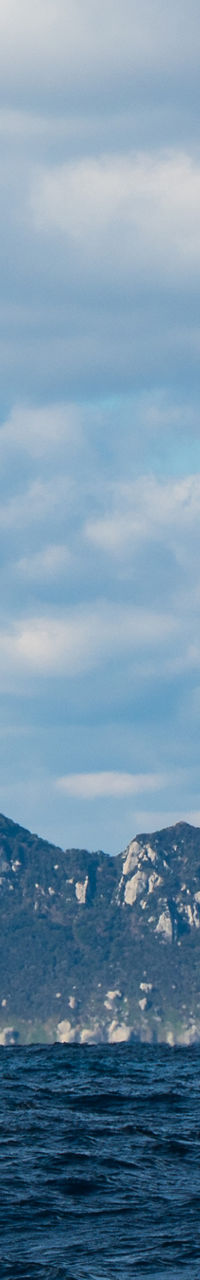 Distant rocky island under cloudy sky and blue sea