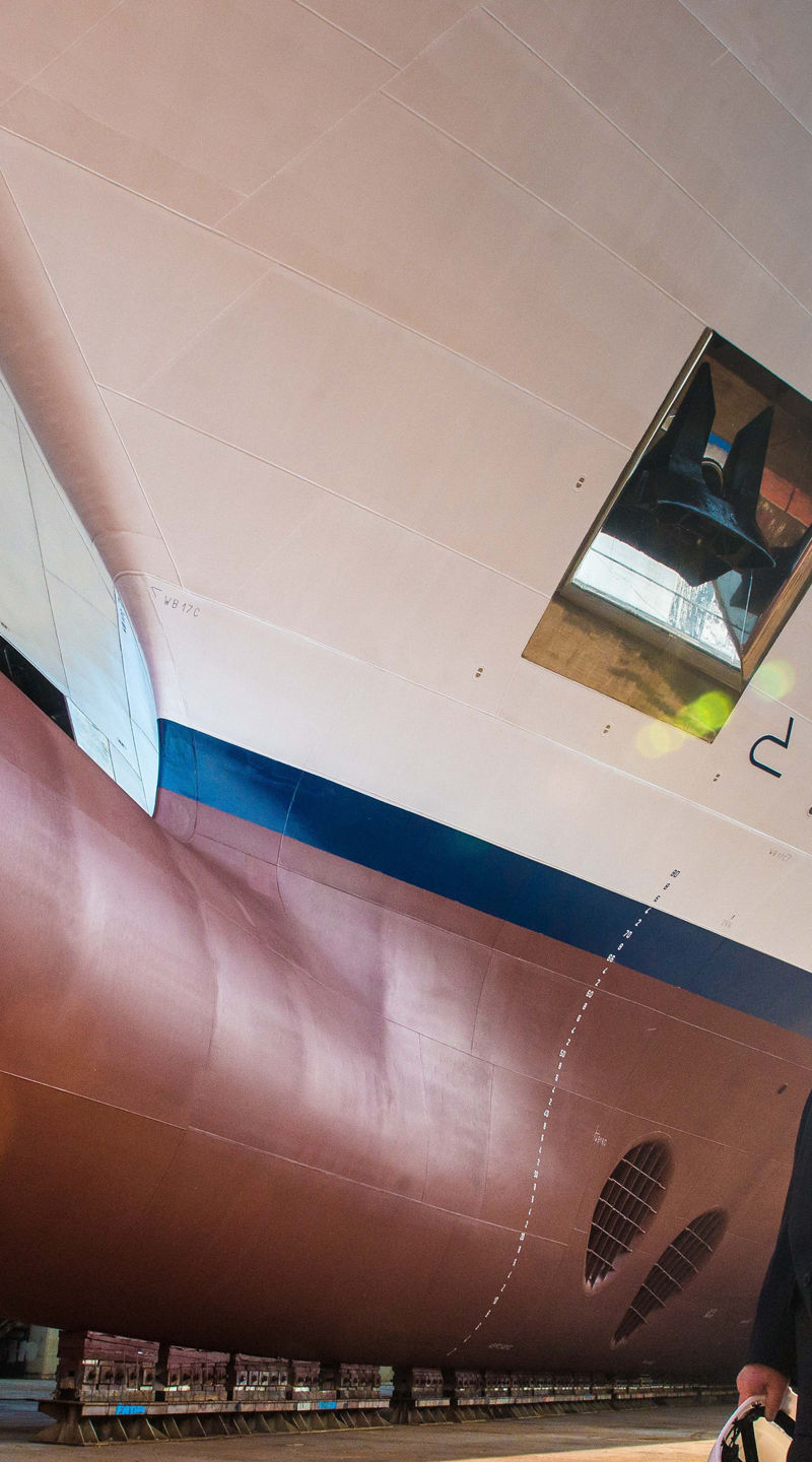 Two people observe large ship in dry dock