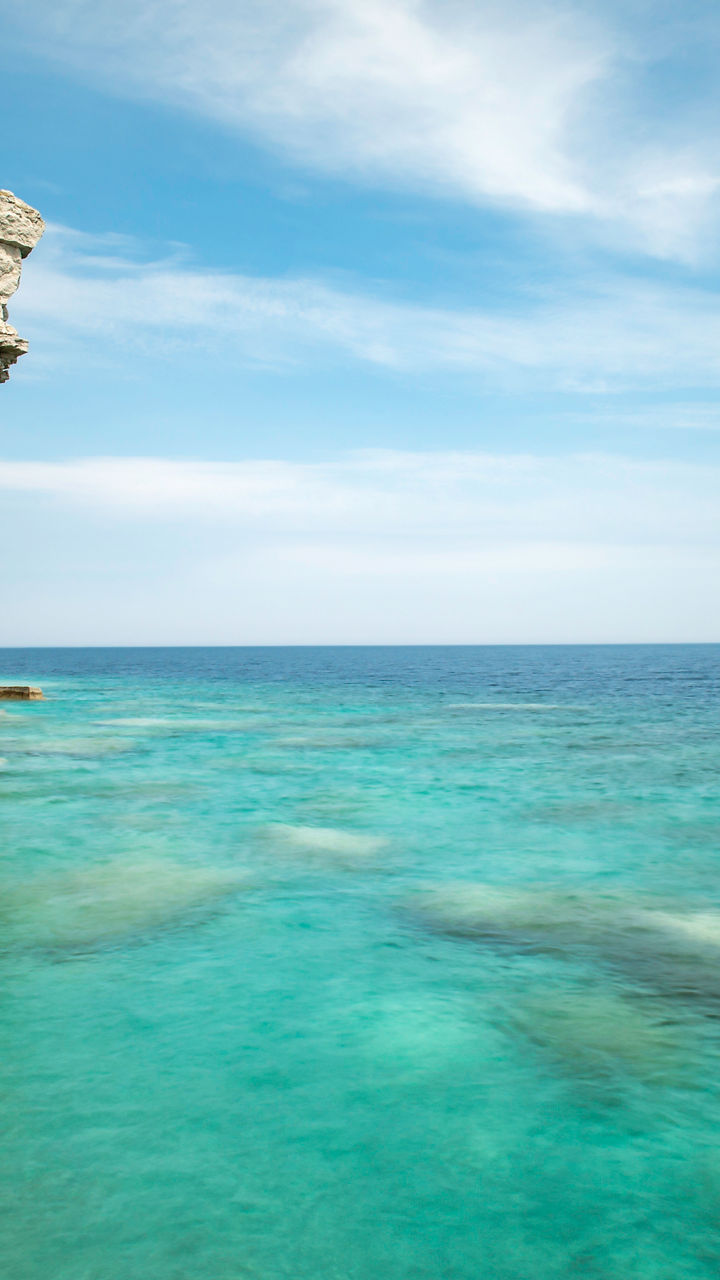 Rock formation by turquoise waters under blue sky