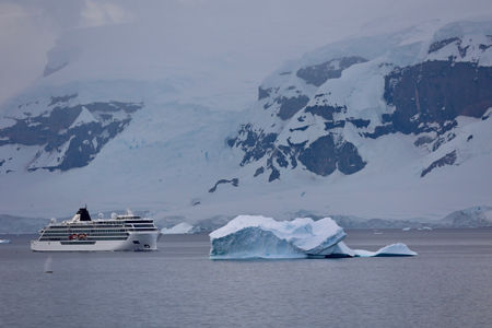 Cruise ship near Antarctic iceberg and snowy cliffs