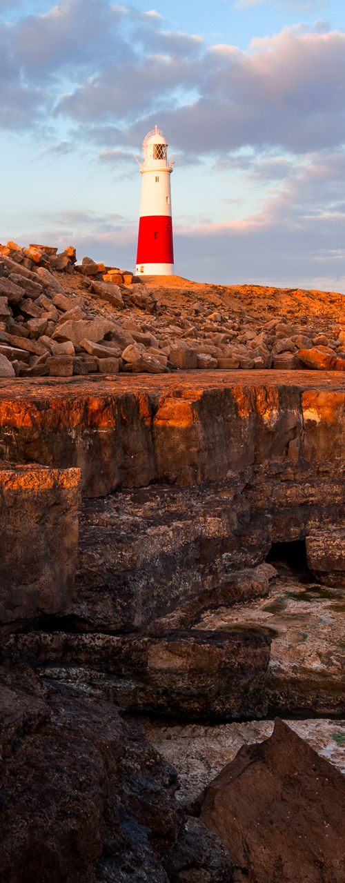 Coastal lighthouse at sunset with rocky shore