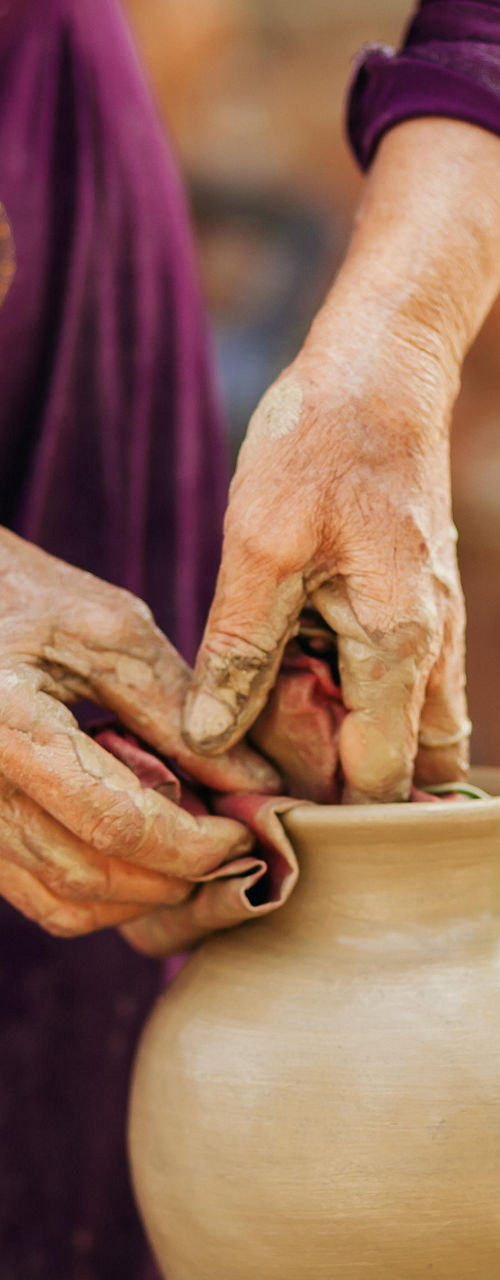 Hands shaping clay pottery outdoors