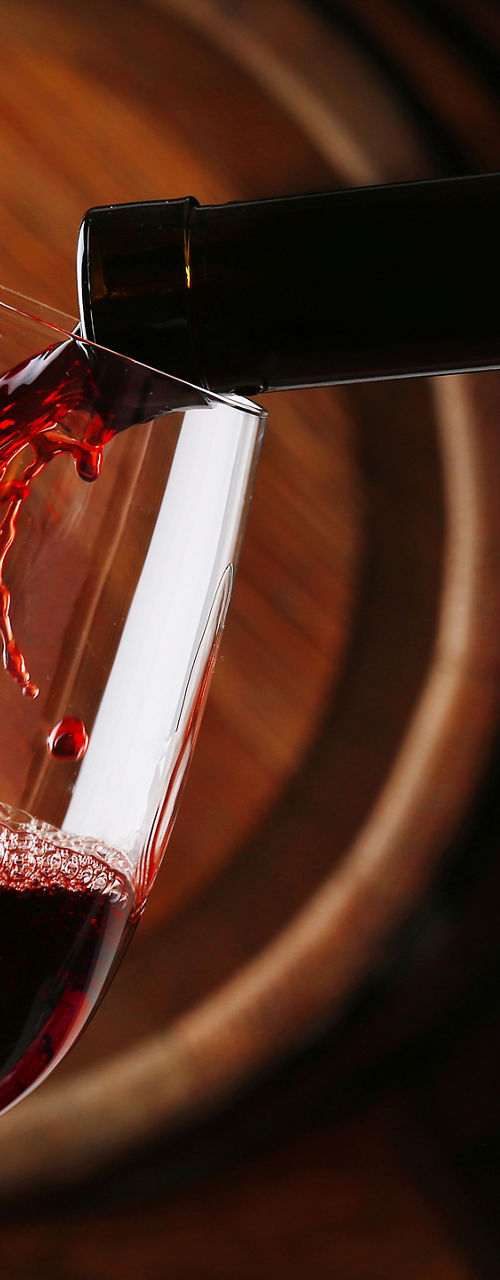 Red wine pouring in glass near barrels