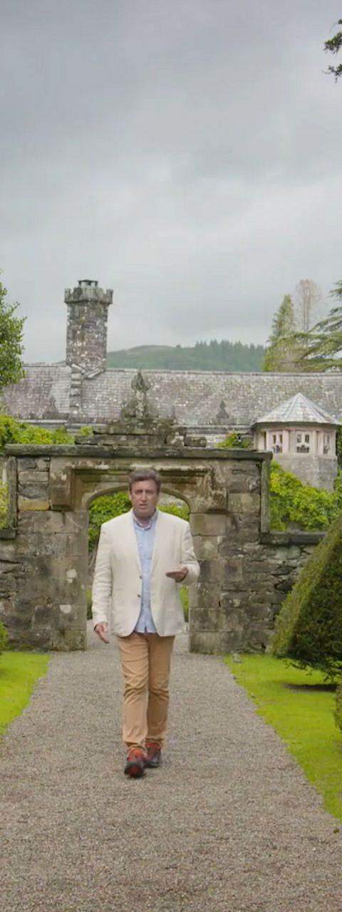 Man walking through formal garden with trimmed hedges